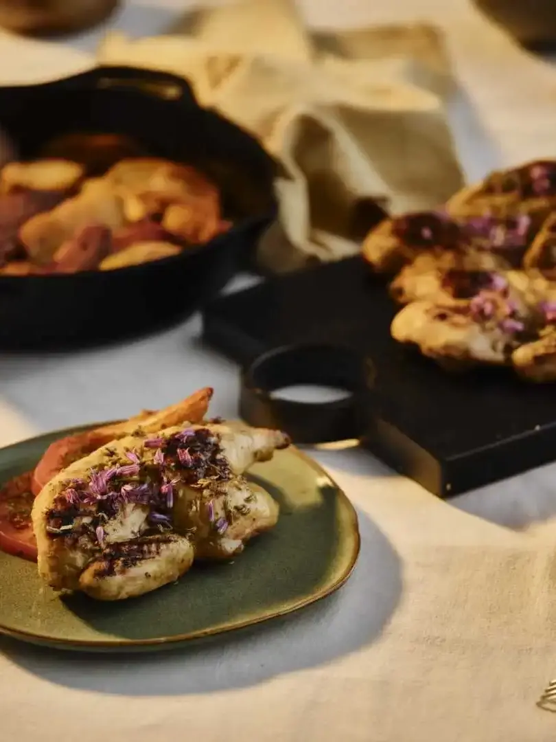 Herb-roasted chicken with edible flowers on a green ceramic plate beside a cast iron skillet at a private dinner catered in Bournemouth
