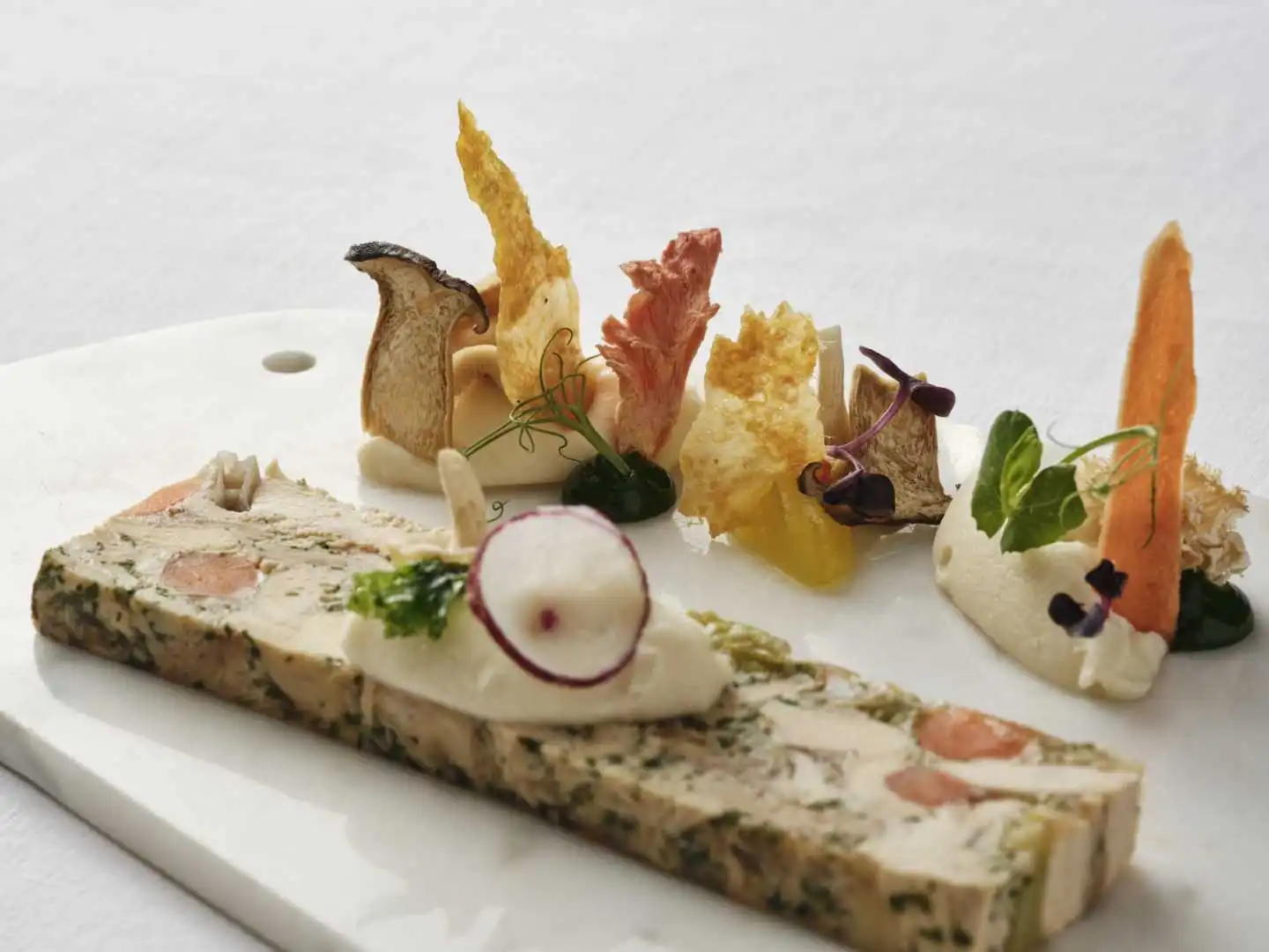 Sliced herb and salmon terrine with cream mousse, radish, vegetable crisps and microgreens on a marble board at a Bournemouth catered event