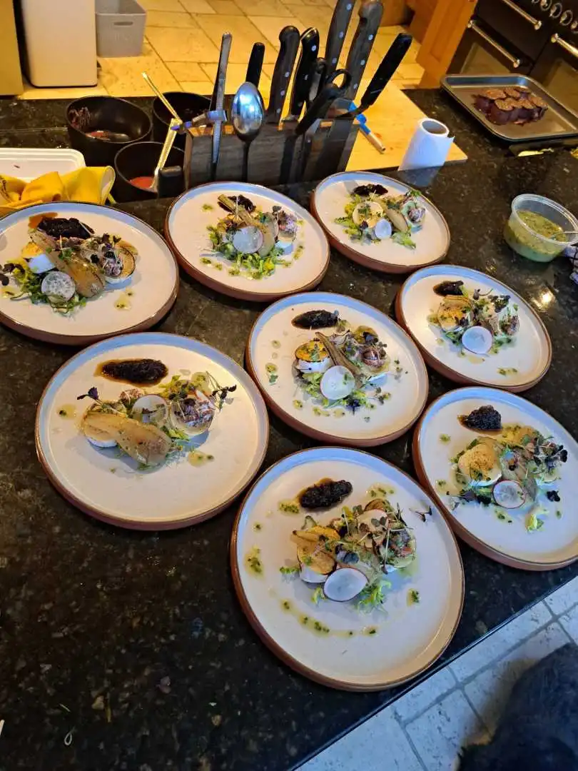 Eight gourmet starter plates being plated simultaneously on a kitchen pass for a private catered dinner event in Bournemouth